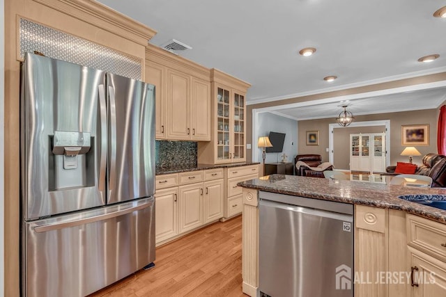 kitchen with backsplash, light hardwood / wood-style floors, stainless steel appliances, dark stone countertops, and ornamental molding