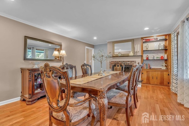 dining space with ornamental molding, a brick fireplace, and light wood-type flooring