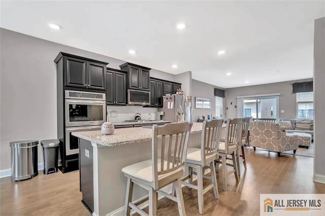 1501 Hights Farm Rd Unit 1501, Monroe, NJ 08831 - kitchen with appliances with stainless steel finishes, open floor plan, a kitchen breakfast bar, a center island with sink, and light wood-style flooring