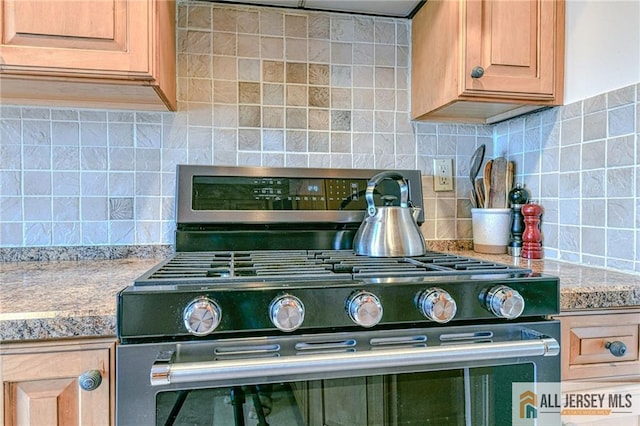 kitchen featuring light stone countertops, stainless steel gas range oven, light brown cabinets, and tasteful backsplash