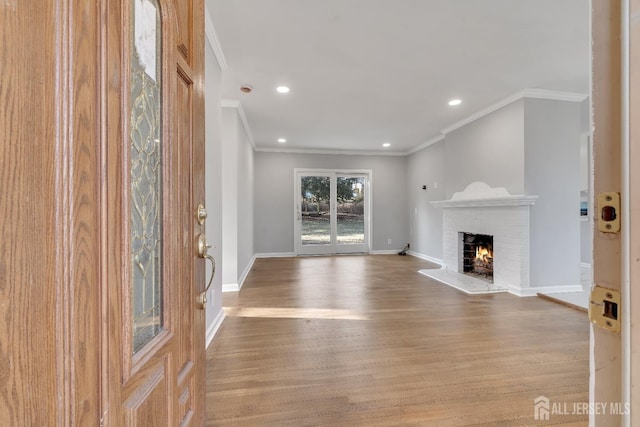 unfurnished living room with recessed lighting, ornamental molding, a brick fireplace, wood finished floors, and baseboards