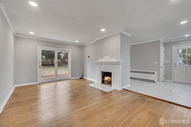 unfurnished living room featuring light hardwood / wood-style floors, a brick fireplace, radiator, and ornamental molding