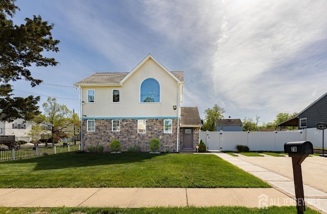 view of front of home featuring stone siding, fence, and a front yard