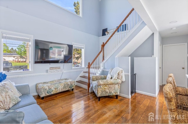 living room with stairway, baseboards, wood finished floors, and a towering ceiling