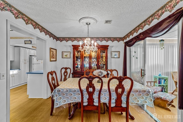 dining area with a textured ceiling, light hardwood / wood-style flooring, and a notable chandelier