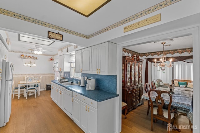 kitchen featuring white appliances, white cabinets, sink, decorative light fixtures, and light hardwood / wood-style floors