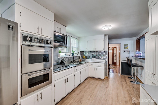 1072 Salem Ave, Hillside, NJ 07205 - kitchen featuring appliances with stainless steel finishes, light wood-style floors, white cabinetry, and tasteful backsplash