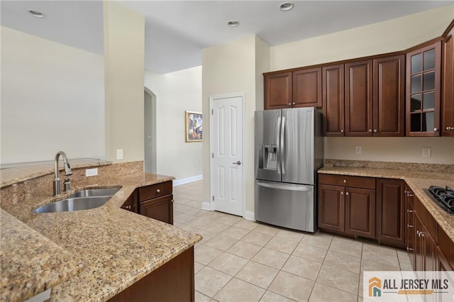 kitchen with light tile patterned flooring, a sink, light stone countertops, stainless steel fridge, and glass insert cabinets