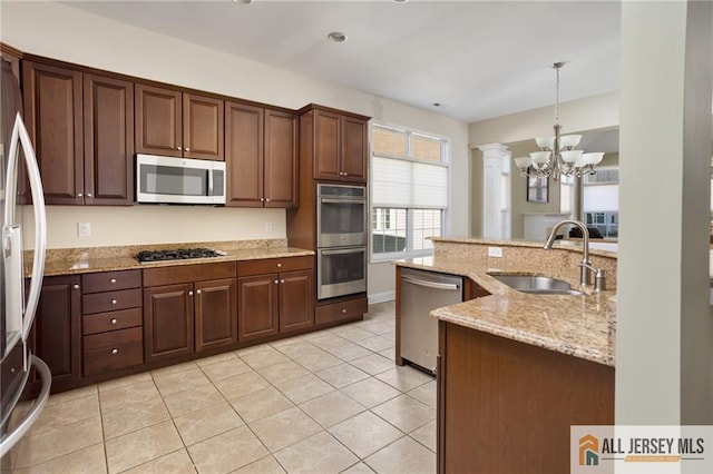 kitchen with appliances with stainless steel finishes, pendant lighting, sink, dark brown cabinetry, and light stone countertops