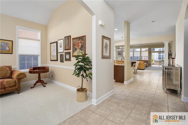 hallway with light tile patterned floors, baseboards, light colored carpet, lofted ceiling, and ornate columns