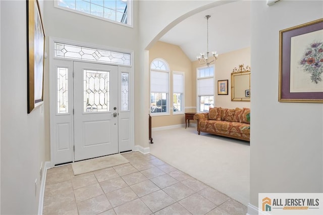 carpeted entryway featuring high vaulted ceiling and a chandelier