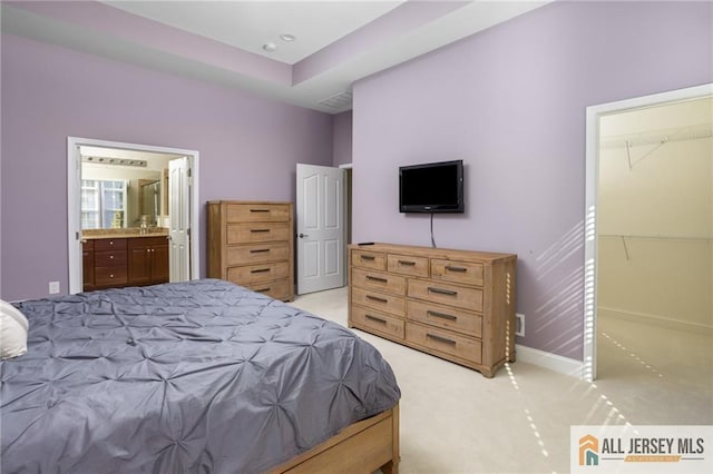 bedroom featuring baseboards, ensuite bathroom, and light colored carpet