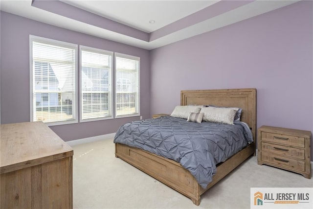 bedroom with light carpet, baseboards, and a raised ceiling