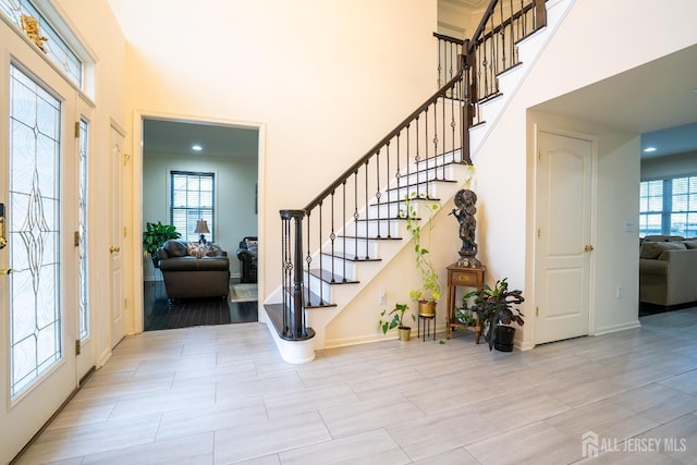 entryway with a towering ceiling, healthy amount of natural light, stairs, and baseboards