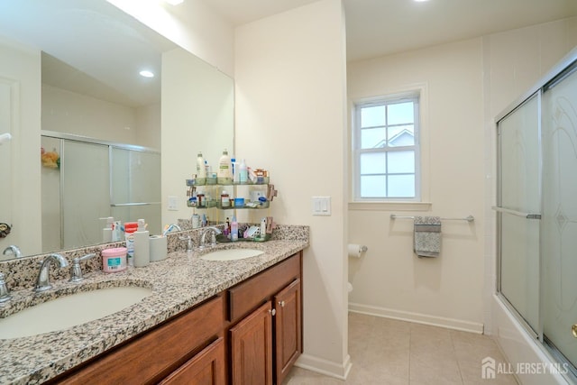 bathroom featuring baseboards, tile patterned floors, double vanity, toilet, and enclosed tub / shower combo