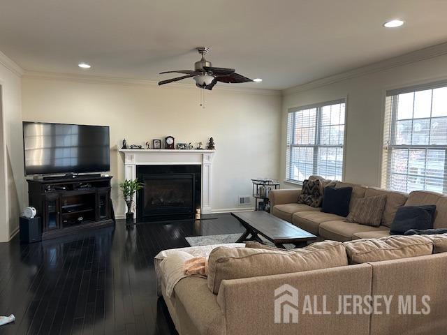 living room featuring a ceiling fan, a glass covered fireplace, recessed lighting, ornamental molding, and hardwood / wood-style floors