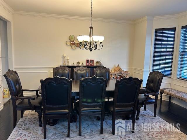 dining space featuring a chandelier, wood finished floors, crown molding, a decorative wall, and a wainscoted wall