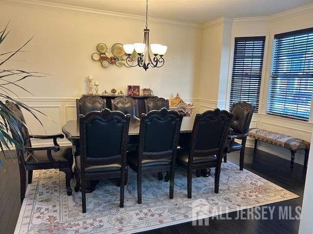 dining area with hardwood / wood-style flooring, a chandelier, a decorative wall, wainscoting, and ornamental molding
