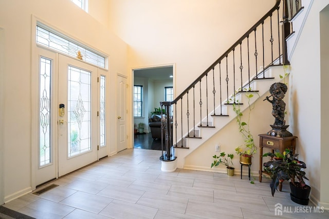 entrance foyer featuring stairs, healthy amount of natural light, a towering ceiling, and baseboards