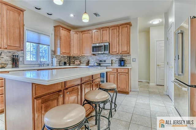 kitchen featuring a breakfast bar, a kitchen island, light countertops, appliances with stainless steel finishes, and hanging light fixtures