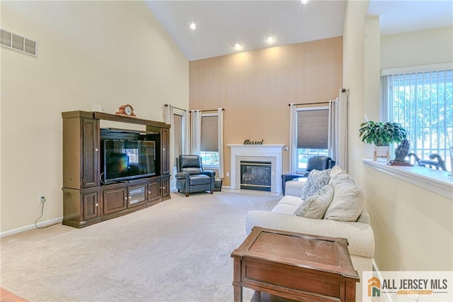 living room with baseboards, visible vents, a glass covered fireplace, light colored carpet, and high vaulted ceiling