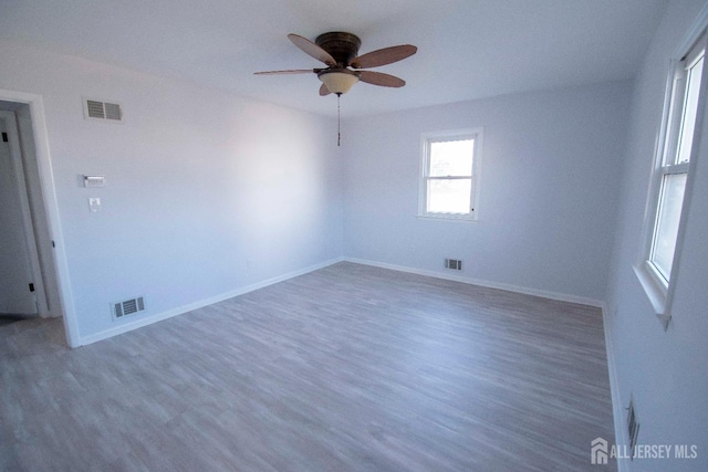 empty room with wood finished floors, visible vents, and baseboards