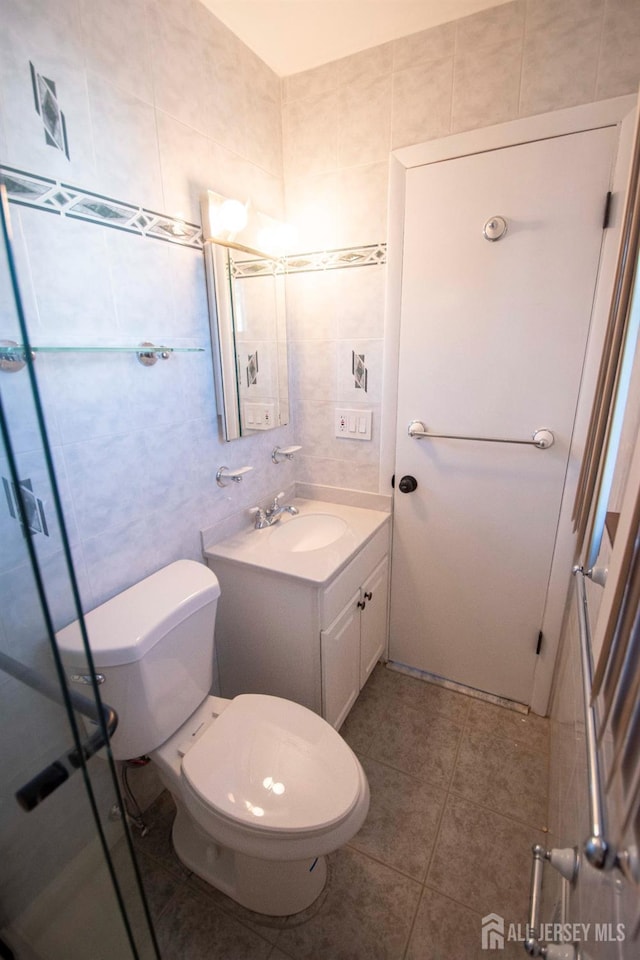 bathroom featuring tile patterned flooring, toilet, vanity, a stall shower, and tile walls