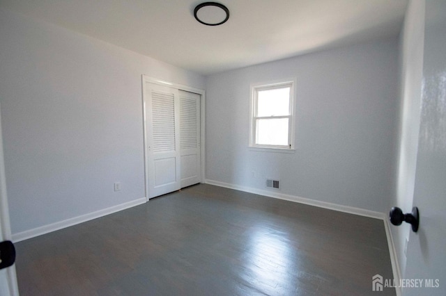 unfurnished bedroom featuring visible vents, baseboards, dark wood-type flooring, and a closet