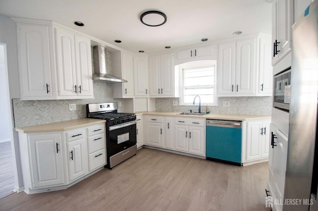 kitchen with light wood-style flooring, a sink, appliances with stainless steel finishes, white cabinets, and wall chimney range hood