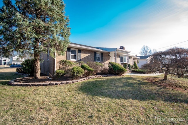 ranch-style home with brick siding, a chimney, and a front yard