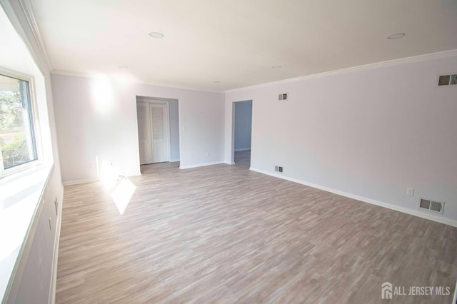 empty room featuring visible vents, light wood-style flooring, baseboards, and ornamental molding