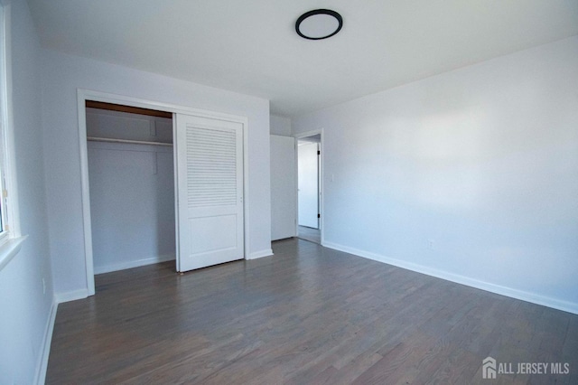 unfurnished bedroom with dark wood finished floors, baseboards, and a closet