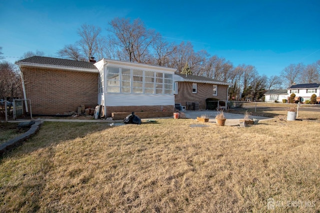 rear view of property with brick siding, a chimney, a yard, and a sunroom