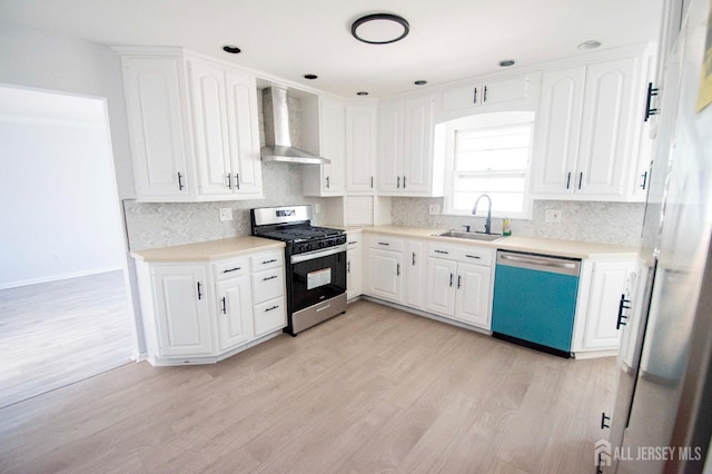 kitchen with stainless steel range with gas cooktop, wall chimney range hood, dishwashing machine, white cabinetry, and a sink