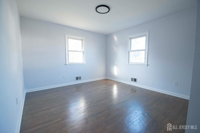 spare room featuring baseboards, visible vents, and dark wood-style flooring