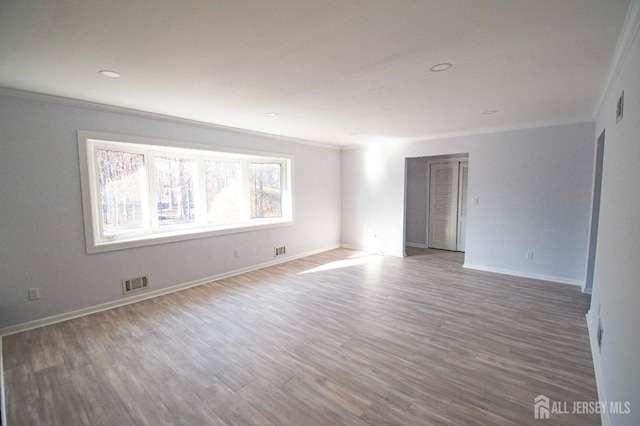 empty room with visible vents, wood finished floors, and ornamental molding