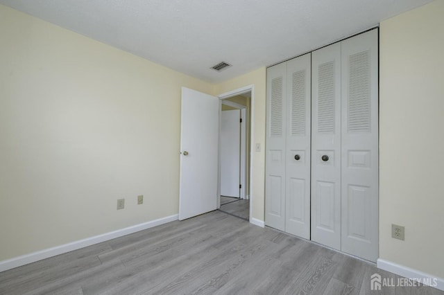 unfurnished bedroom featuring baseboards, visible vents, light wood finished floors, and a closet