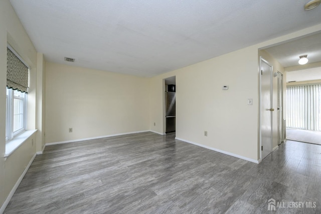 spare room featuring visible vents, baseboards, plenty of natural light, and wood finished floors
