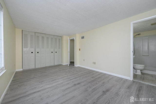 unfurnished bedroom featuring visible vents, baseboards, a textured ceiling, and wood finished floors