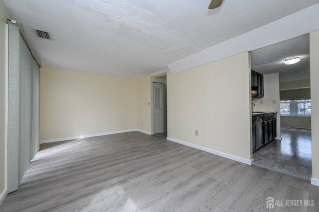 unfurnished living room with a textured ceiling, baseboards, visible vents, and wood finished floors