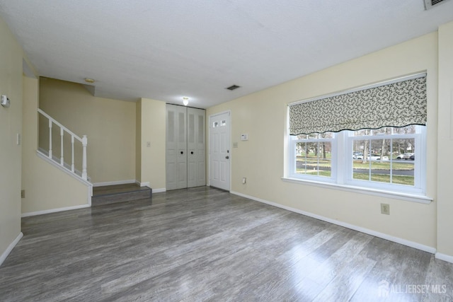 unfurnished living room featuring baseboards, stairs, wood finished floors, and visible vents