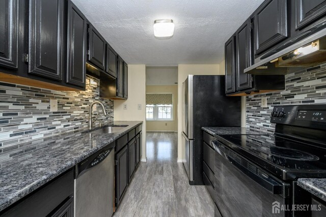 kitchen featuring electric range, stainless steel dishwasher, a sink, dark cabinets, and under cabinet range hood