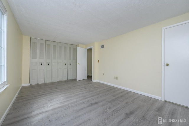 unfurnished bedroom featuring baseboards, a textured ceiling, wood finished floors, and visible vents