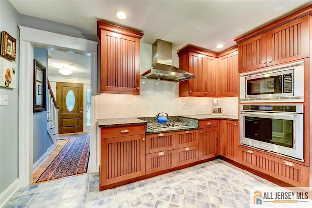 kitchen with tasteful backsplash, dark stone countertops, wall chimney range hood, and appliances with stainless steel finishes