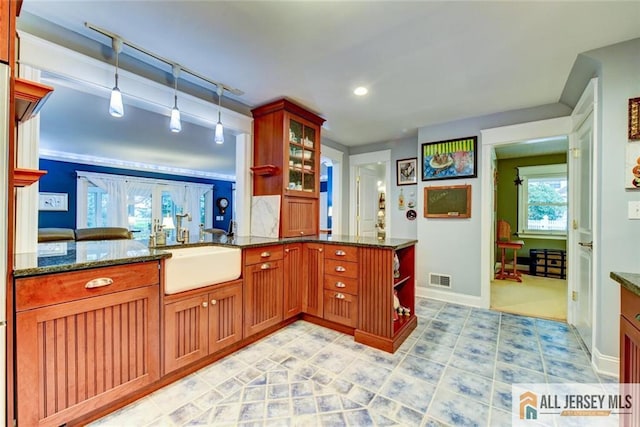 kitchen with pendant lighting, kitchen peninsula, sink, and dark stone counters