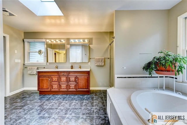 bathroom with a skylight, vanity, and a relaxing tiled tub