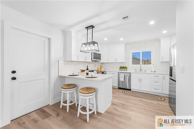 737 Prospect Rd Unit 737A, Monroe, NJ 08831 - kitchen with stainless steel appliances, light wood-type flooring, white cabinets, backsplash, and a peninsula
