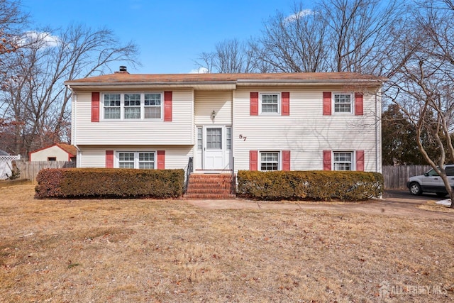 split foyer home featuring entry steps, fence, and a front lawn