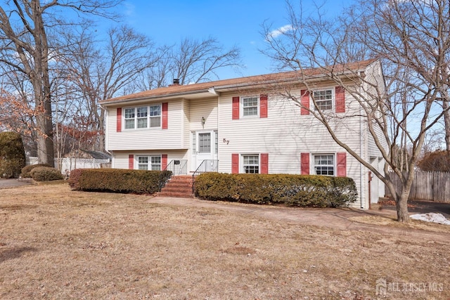 bi-level home featuring a front yard, fence, and a chimney