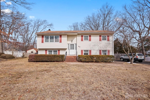 bi-level home featuring a chimney, a front yard, and fence